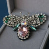 A handcrafted rhinestone bee sew-on patch with sparkling wings and a pink center set against a gray background.
