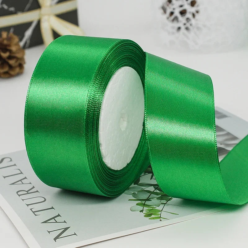 A roll of vibrant green satin ribbon lying on a sheet of paper with a green leaf design.