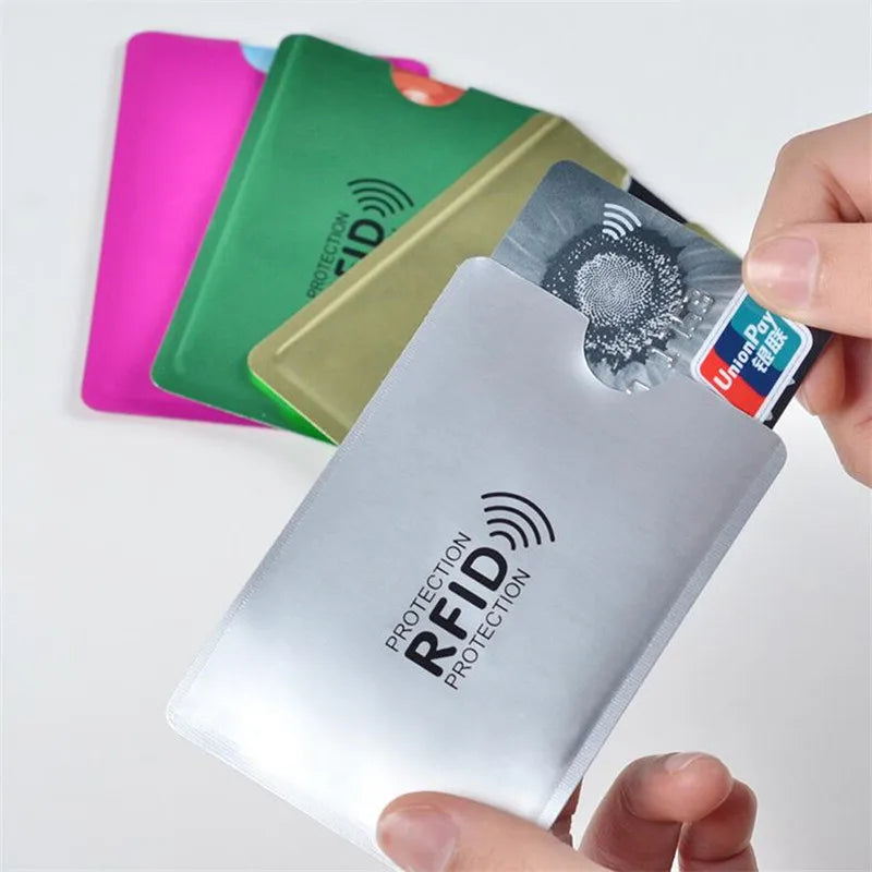 A hand holds a silver RFID blocking aluminum card holder next to several colored plastic cards.
