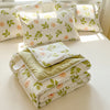 A set of white and green floral patterned pillows and a folded duvet cover with lace trim on a light surface.