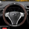 A close-up view of a Nissan steering wheel with a brown carbon fiber patterned grip cover.