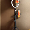 A black tripod holds a ring light with an orange glow and a smartphone mounted on it.