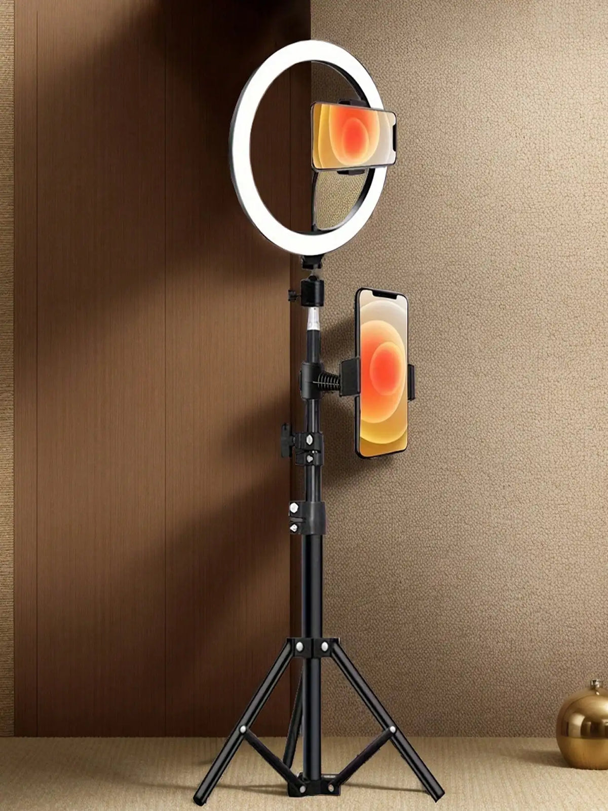 A black tripod holds a ring light with an orange glow and a smartphone mounted on it.