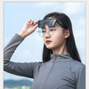 A woman wearing black clip-on sunglasses with thin metal frames and a gray zip-neck athletic jacket outdoors.