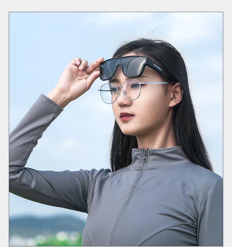 A woman wearing black clip-on sunglasses with thin metal frames and a gray zip-neck athletic jacket outdoors.