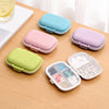 A set of eight pastel-colored pill organizers and a clear compartment organizer displayed on a wooden table.