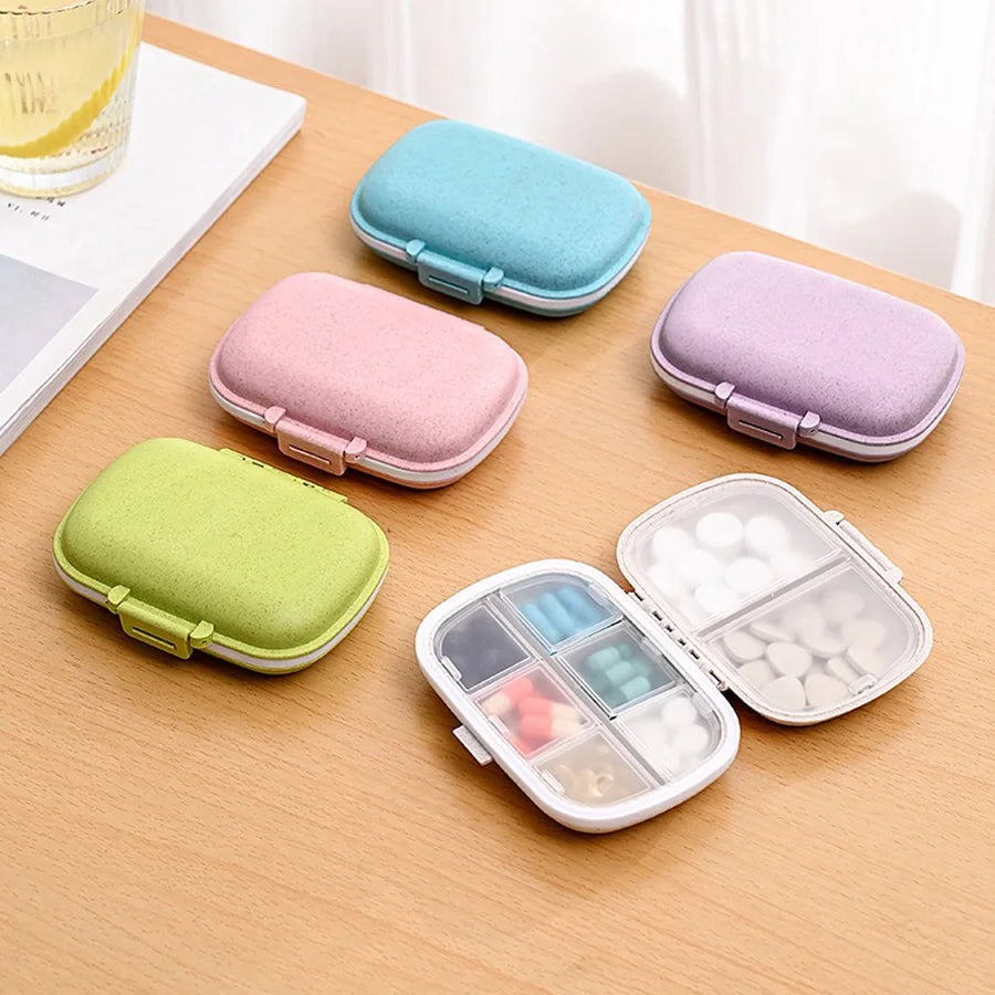A set of eight pastel-colored pill organizers and a clear compartment organizer displayed on a wooden table.