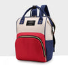 A beige and navy insulated canvas mummy diaper bag with a red front pocket and hanging hook.