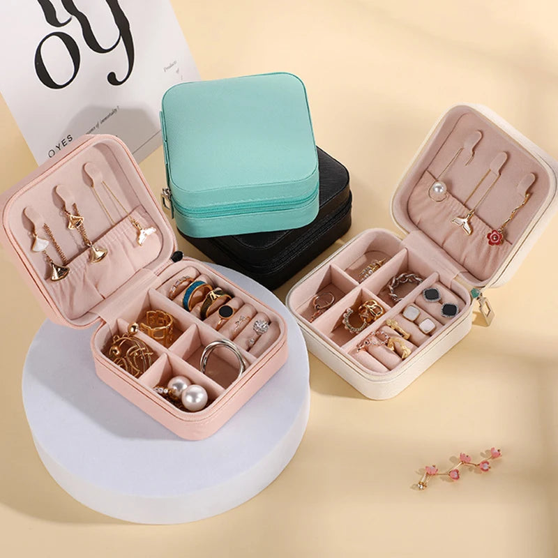 A pink PU leather jewelry storage box with compartments and a teal storage pouch and jewelry displayed.