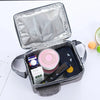 Silver insulated lunch bag with a clear lid containing various small items like a cosmetic jar and a dark phone.
