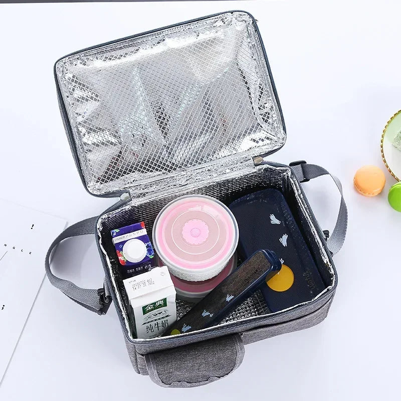 Silver insulated lunch bag with a clear lid containing various small items like a cosmetic jar and a dark phone.