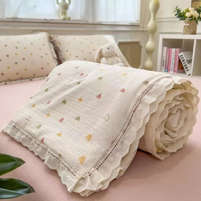 A rolled beige floral washed cotton gauze summer quilt with embroidered hearts and small flowers.