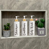 Three white refillable shampoo and lotion dispenser bottles with yellow pump tops and green cactus accents displayed in a woo