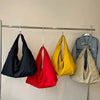 Four lightweight nylon tote bags in black, red, yellow, and beige hanging on a metal rack.