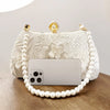 A white pearl embroidered evening clutch with a gold chain and a smartphone resting on it.