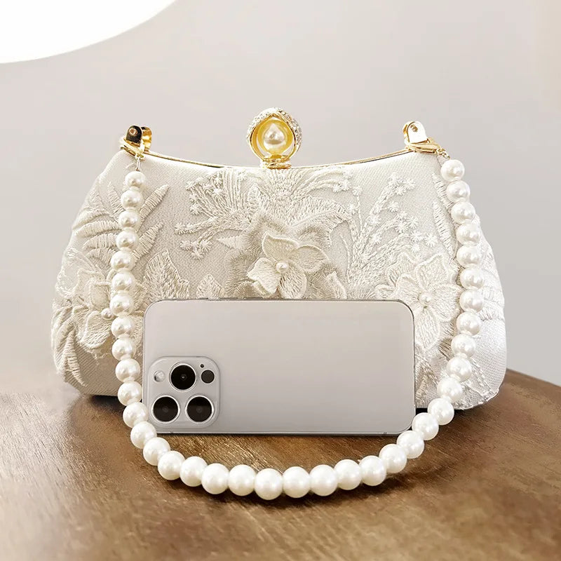 A white pearl embroidered evening clutch with a gold chain and a smartphone resting on it.