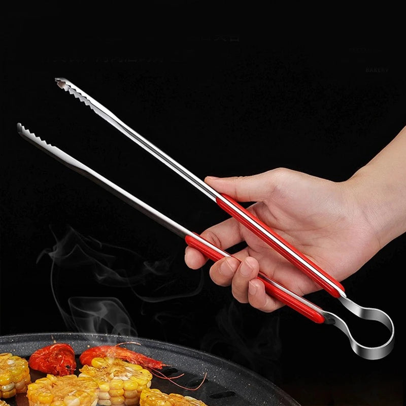 A hand holds a pair of shiny stainless steel BBQ tongs over grilled food on a dark pan.