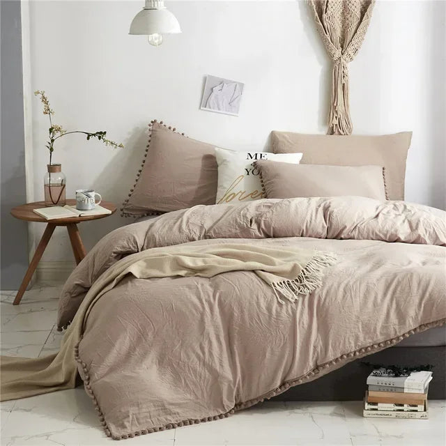 A beige duvet cover set with pom tassels on a bed, featuring soft microfiber bedding.