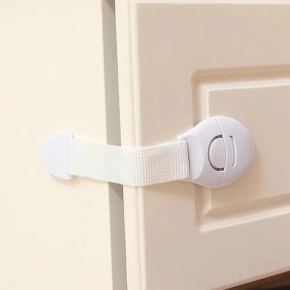 A white child safety cabinet lock is installed on a light beige cabinet door.