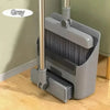 A grey folding broom and dustpan set with an aluminum handle resting on a wooden floor.