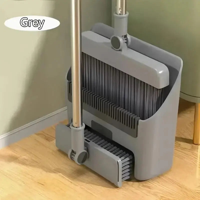 A grey folding broom and dustpan set with an aluminum handle resting on a wooden floor.