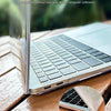 A close-up of a silver laptop edge protected by an inclusive design case on a wooden surface.