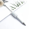A silver ballpoint pen with a sparkly diamond sequin filling is shown next to some dried grass and a light beige object.