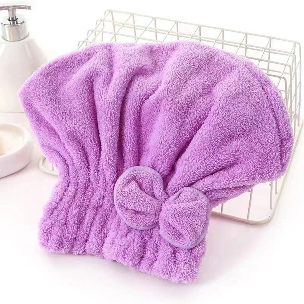 A purple microfiber hair drying towel with a bow-knot head wrap displayed in a wire basket.