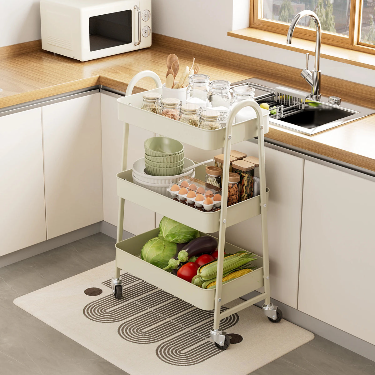 A white 3-tier rolling metal storage cart filled with various kitchen items on a countertop.