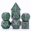 A set of seven metal polyhedral dice in gray with green dragon font designs, including a pyramid and cubes.