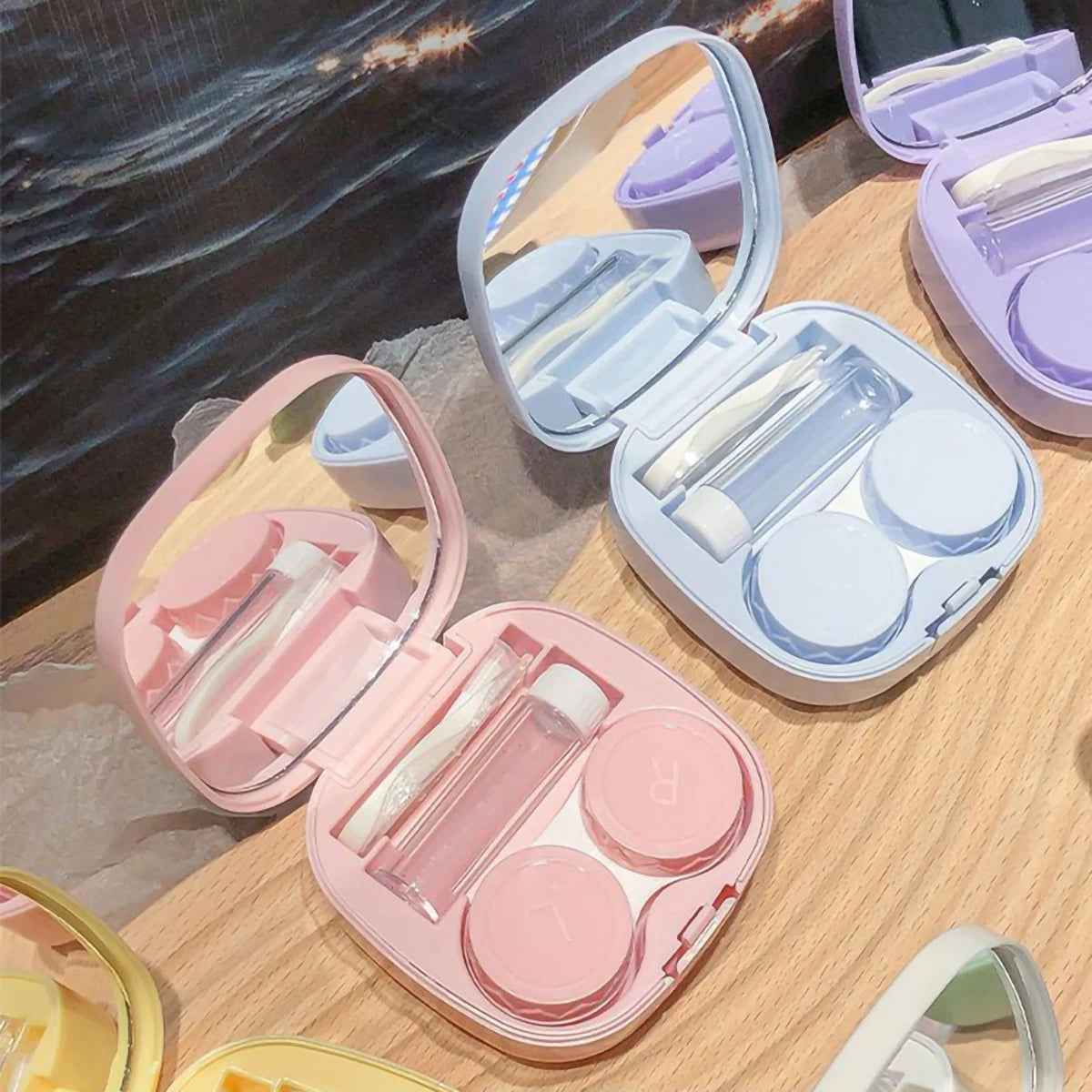 A collection of pink and purple compact contact lens travel cases with secure closures displayed on a wooden surface.