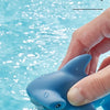 A hand is squeezing a blue turtle and shark floating bath toy, which is spraying water.