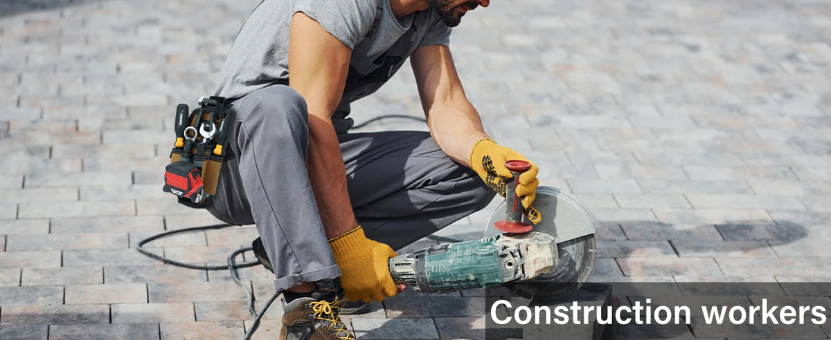A construction worker wearing a grey shirt and pants is using a handheld power tool on a brick surface.