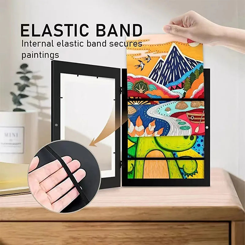 An elastic band secures paintings inside a black photo display frame.