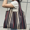 A person is holding a brown and beige striped foldable oxford cloth tote bag against a light gray wall.