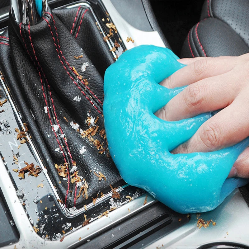 A hand is squeezing a bright blue reusable cleaning gel onto a car interior surface.