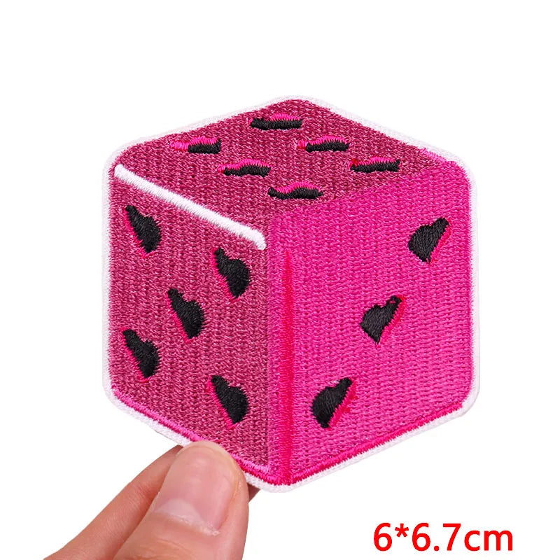 A pink felt cube with black embroidered patches, measuring 6x6.7 cm.