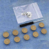 A small silver snap button kit is displayed on a translucent plastic bag on a blue denim fabric.