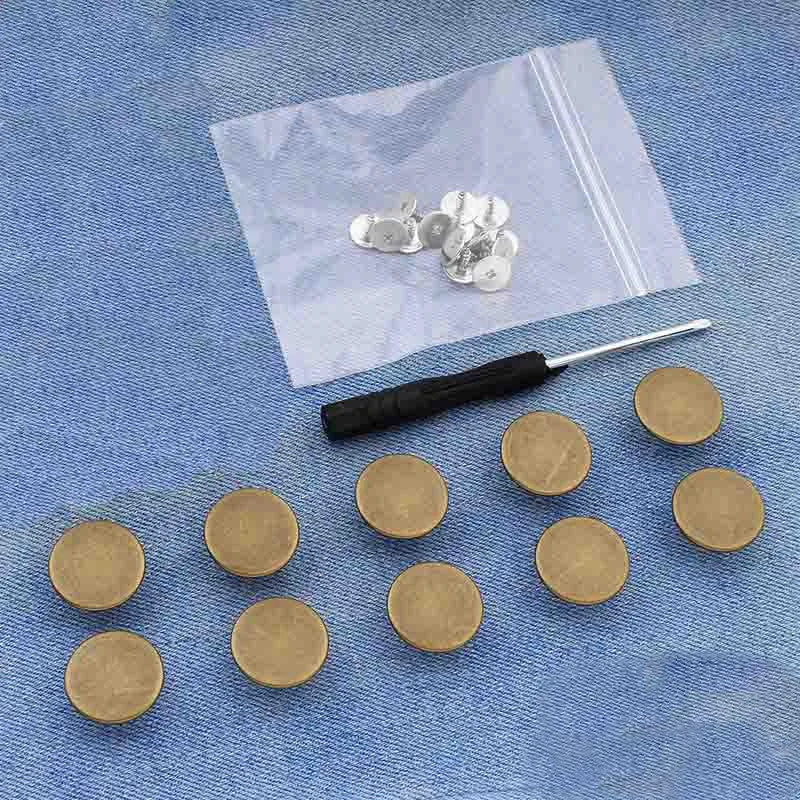 A small silver snap button kit is displayed on a translucent plastic bag on a blue denim fabric.