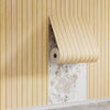 Vertical striped wallpaper featuring light beige and gold tones on a wall with a rolled-up section.