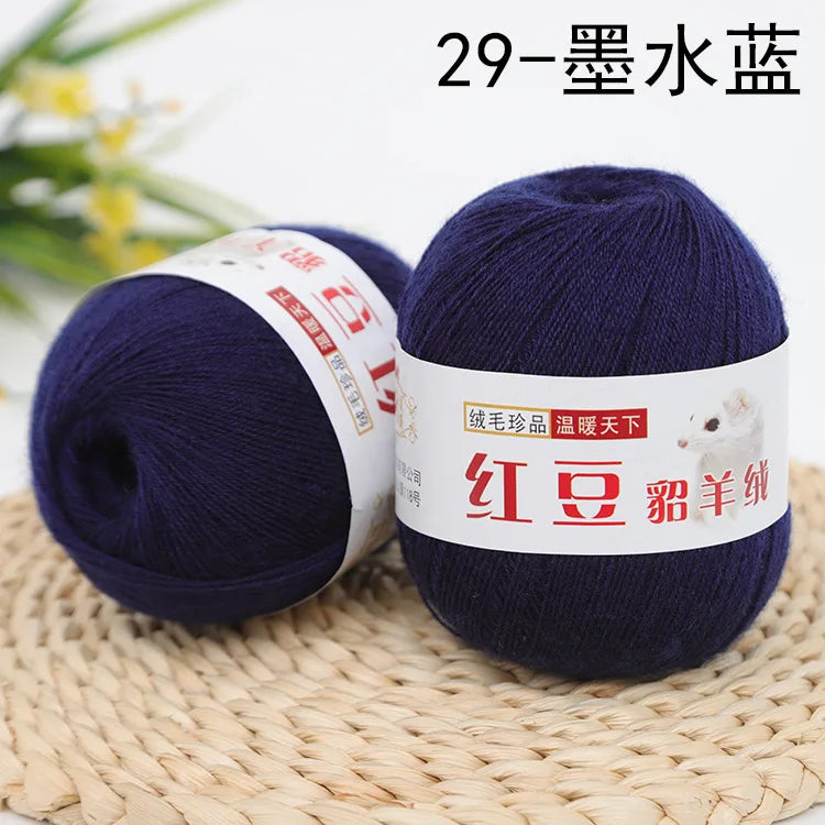 A dark blue ball of yarn labeled as 29-gauge wool yarn for knitting and crochet resting on a woven mat.