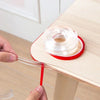 Hands are installing transparent silicone corner guards onto a wooden table edge for baby safety.