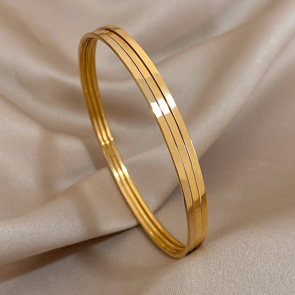 A stack of four thin gold-plated stainless steel bangles displayed on a neutral fabric background.