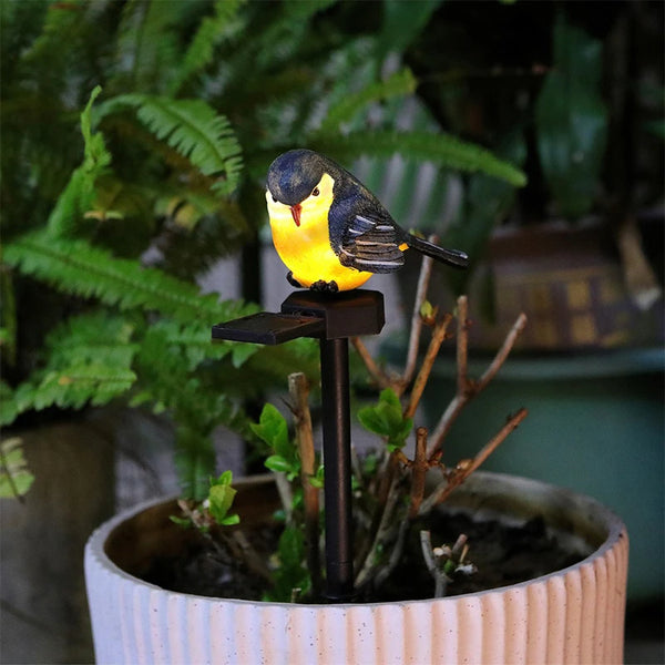A solar-powered resin bird garden stake light with a black post and yellow bird decoration planted in soil.