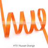 A strand of rust orange satin ribbon is shown coiled and unwound against a white background.