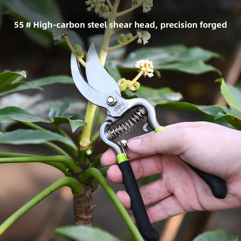 A hand holds a precision forged steel shear head, used for pruning, against a background of green foliage.