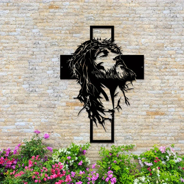 Silhouette noire de la tête et de la barbe de Jésus dans une croix montée sur un mur de pierre avec des fleurs colorées en de