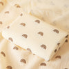 A beige soft cotton gauze baby swaddle blanket with a repeating brown rainbow pattern is displayed on a light fabric.