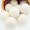 A set of three white natural wool dryer balls nestled in a woven basket.