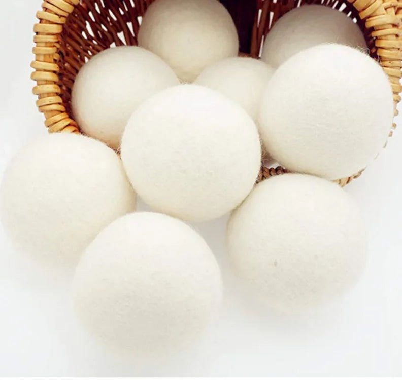 A set of three white natural wool dryer balls nestled in a woven basket.